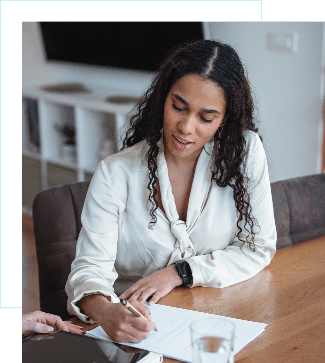 Woman signing documents at a wooden table.